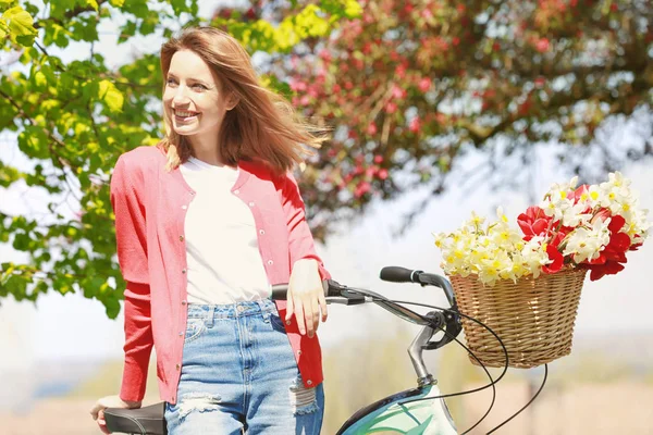 Ung vacker flicka nära cykel med blommor i korg på park solig dag — Stockfoto