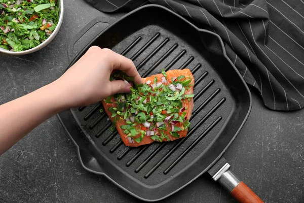 Woman sprinkling salmon fillet with herbs — Stock Photo, Image