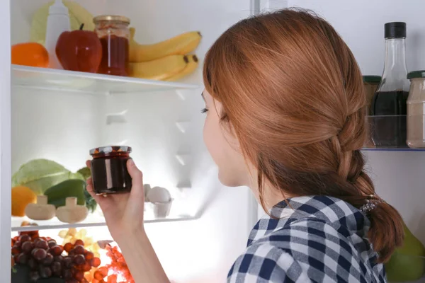 Ung flicka tar burken med sås från kylskåpet — Stockfoto