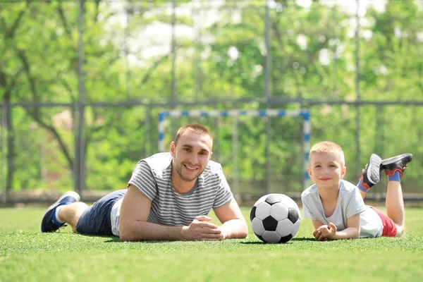 Отец и сын с мячом лежат на футбольном поле — стоковое фото