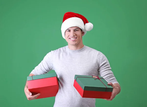 Красивий чоловік у різдвяній шапці тримає подарункові коробки на кольоровому фоні — стокове фото