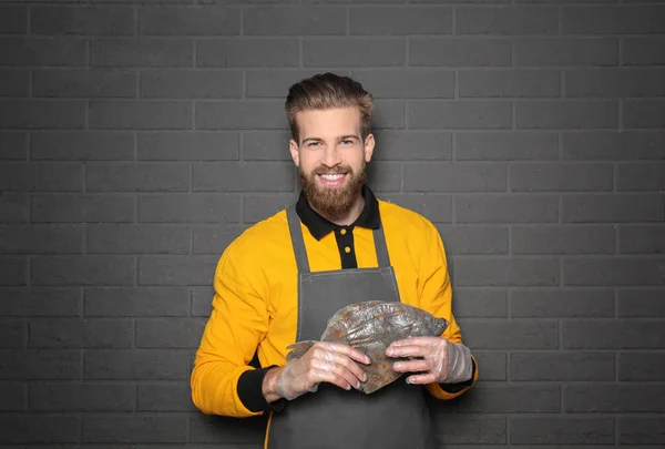 Handsome seller holding fresh fish on gray wall background — Stock Photo, Image