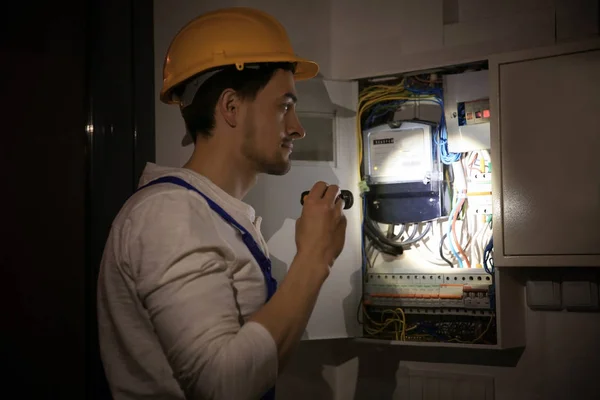 Joven electricista con linterna cerca de la caja de interruptores en habitación oscura —  Fotos de Stock