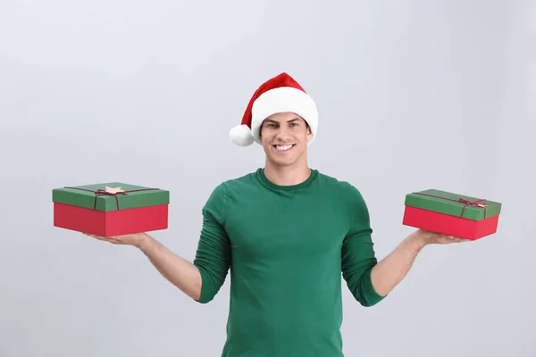 Красивий чоловік у різдвяній шапці тримає подарункові коробки на світлому фоні — стокове фото