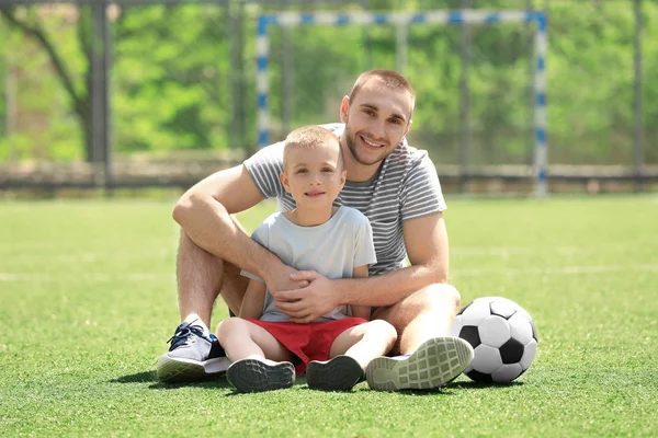 Отец и сын с мячом сидят на футбольном поле — стоковое фото