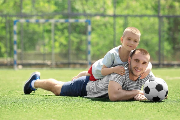 Padre e hijo con la pelota acostado en el campo de fútbol —  Fotos de Stock