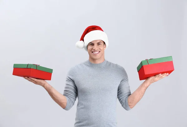 Bello uomo in cappello di Natale che tiene scatole regalo su sfondo chiaro — Foto Stock
