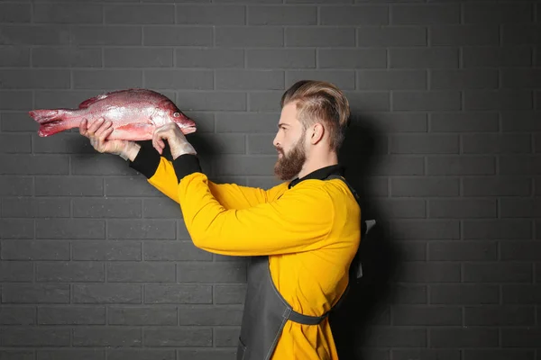 Красивый продавец держит свежую рыбу на сером фоне стены — стоковое фото
