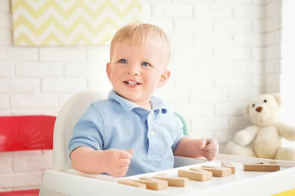 Schattige kleine jongen spelen met houten letters zittend in kinderstoel — Stockfoto