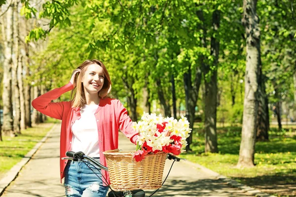 Flicka och cykel med blommor i korg — Stockfoto