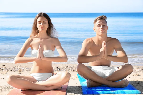 Pareja practicando yoga en la playa de mar — Foto de Stock