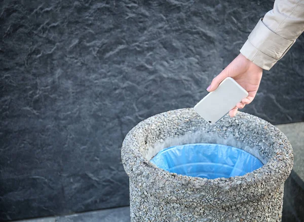 Woman throwing phone into stone bin