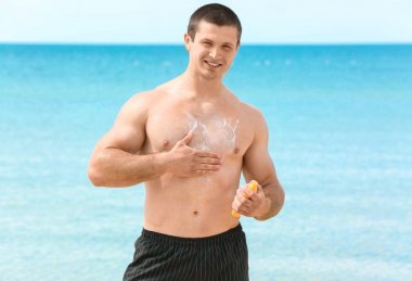 Deniz sahilinde güneş kremi süren yakışıklı genç adam.