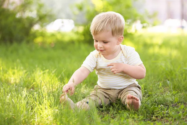 Ładny chłopczyk siedzi na zielonej trawie — Zdjęcie stockowe