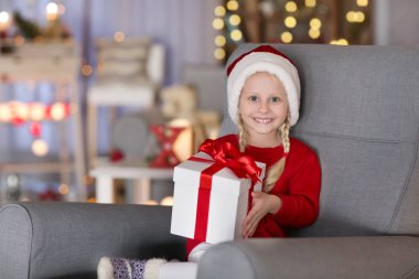 Sevimli küçük kız evde koltukta oturan Noel hediye kutusu ile