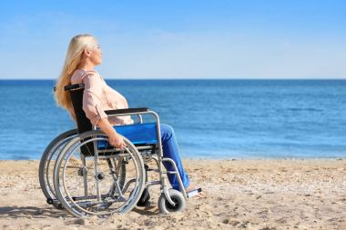 Deniz kıyısında tekerlekli sandalyede yaşlı kadın