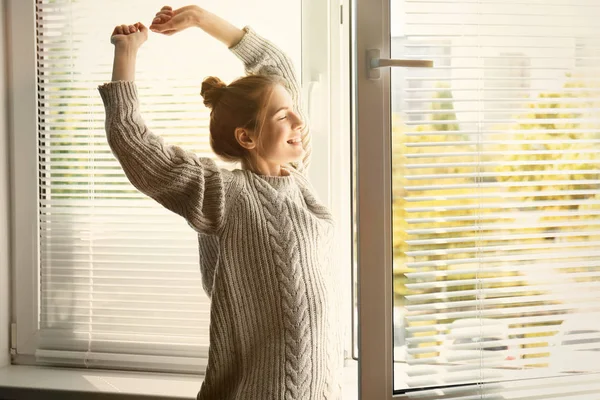 Счастливая молодая девушка растягивается у окна дома — стоковое фото