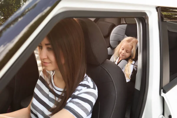 Молода жінка водить машину з маленькою дівчинкою на сидінні безпеки — стокове фото
