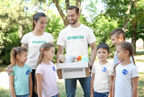 Jóvenes voluntarios y niños con caja de donaciones al aire libre — Foto de Stock