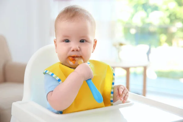 Cute baby with spoon sitting in kitchen — Stock Photo, Image