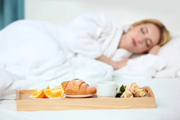 Tray with breakfast in hotel room and sleeping woman on background