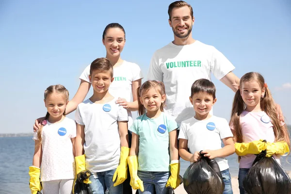 Jóvenes voluntarios y niños con bolsas de basura en la playa —  Fotos de Stock
