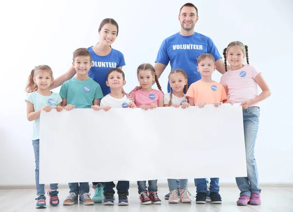Mutlu gönüllüler ve çocukları boş poster holding — Stok fotoğraf
