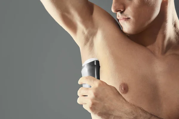 Pohledný mladý muž s deodorant na šedém pozadí — Stock fotografie