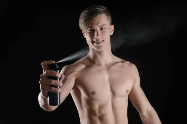 Handsome young man with deodorant on dark background — Stock Photo, Image