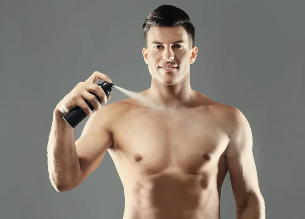 Handsome young man with deodorant on grey background