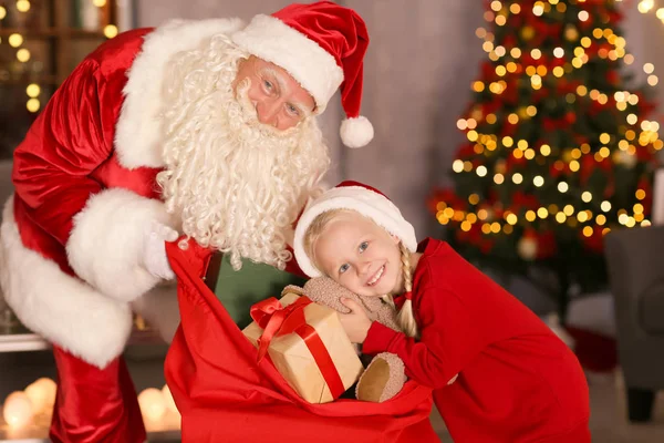 Little girl choosing present from Santa\'s gift bag in decorated room