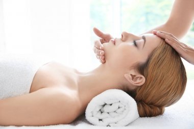 Genç bir kadın spa salonunda yüz masajından hoşlanıyor.