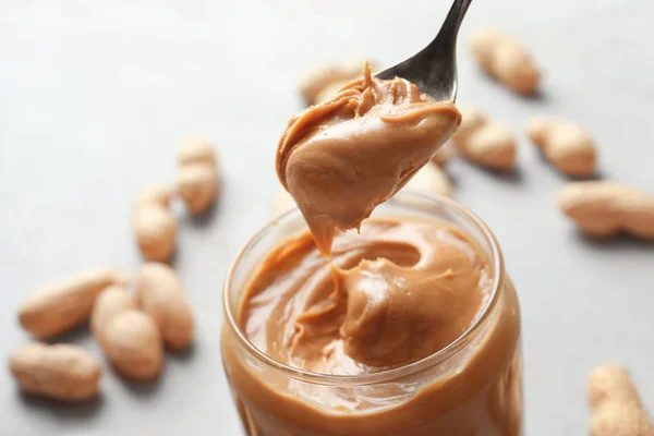 Peanut butter in spoon and jar — Stock Photo, Image