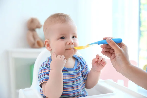Mother feeding baby with spoon indoors — Stock Photo, Image