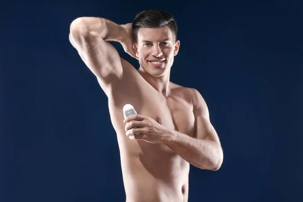 Pohledný mladý muž s deodorant na tmavě modrém pozadí — Stock fotografie