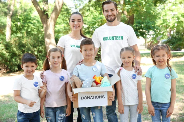 Jóvenes voluntarios y niños con caja de donaciones al aire libre — Foto de Stock