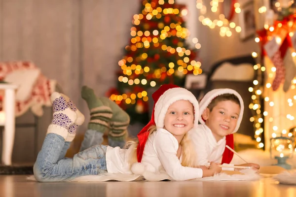 Lindos niños escribiendo carta a Santa en la habitación decorada para Navidad —  Fotos de Stock