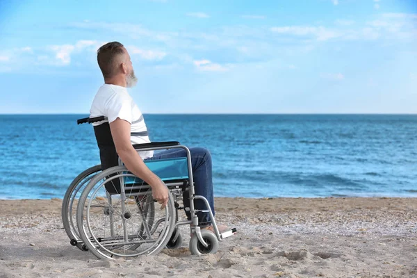 Deniz kıyısında tekerlekli sandalyede yaşlı bir adam.