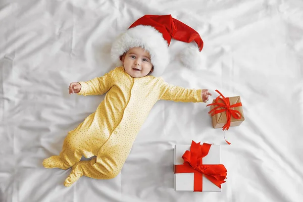 Bebê bonito em chapéu de Papai Noel e caixas de presente em folha branca — Fotografia de Stock