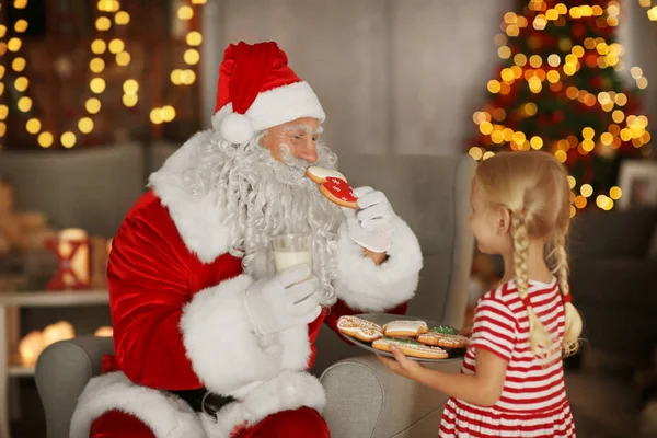 Liten flicka att behandla Santa med välsmakande kakor och mjölk i rum med vackra juldekorationer — Stockfoto