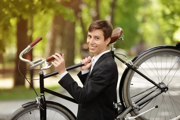Joven hombre de negocios guapo sosteniendo bicicleta en el hombro, al aire libre — Foto de Stock