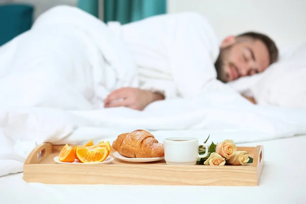 Tray with breakfast in hotel room and sleeping man on background — Stock Photo, Image