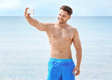 Deniz sahilinde selfie çeken yakışıklı genç adam.