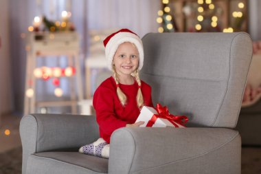 Sevimli küçük kız evde koltukta oturan Noel hediye kutusu ile