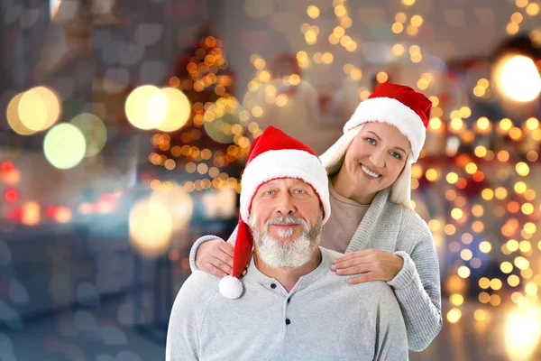 Senior coppia felice in Santa cappelli su sfondo luci di Natale sfocate — Foto Stock