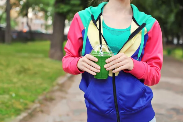 Woman in sport suit walking outdoors with green smoothie