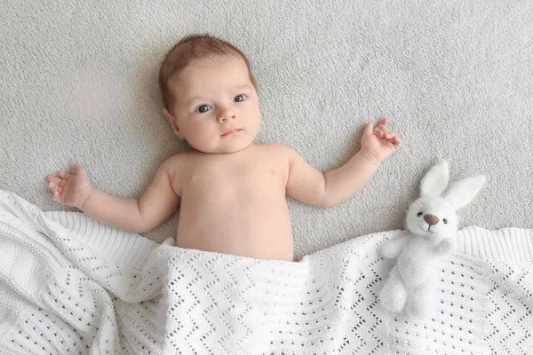 Bebê bonito com brinquedo deitado em xadrez macio em casa — Fotografia de Stock