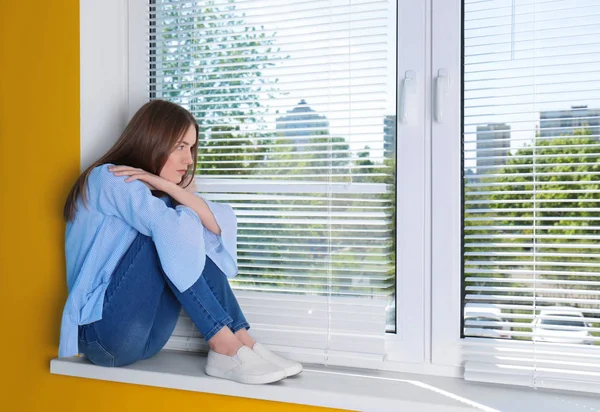 Belle fille triste assise sur le rebord de la fenêtre à la maison — Photo