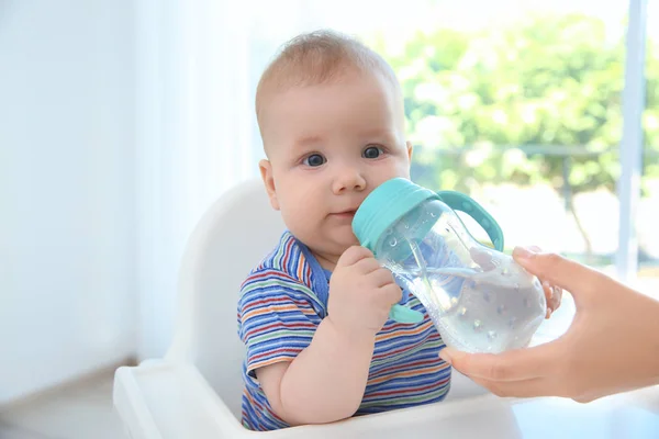 Mother giving baby bottle with water indoors — Stock Photo, Image