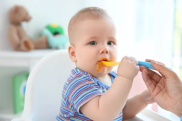 Mother feeding baby with spoon indoors — Stock Photo, Image